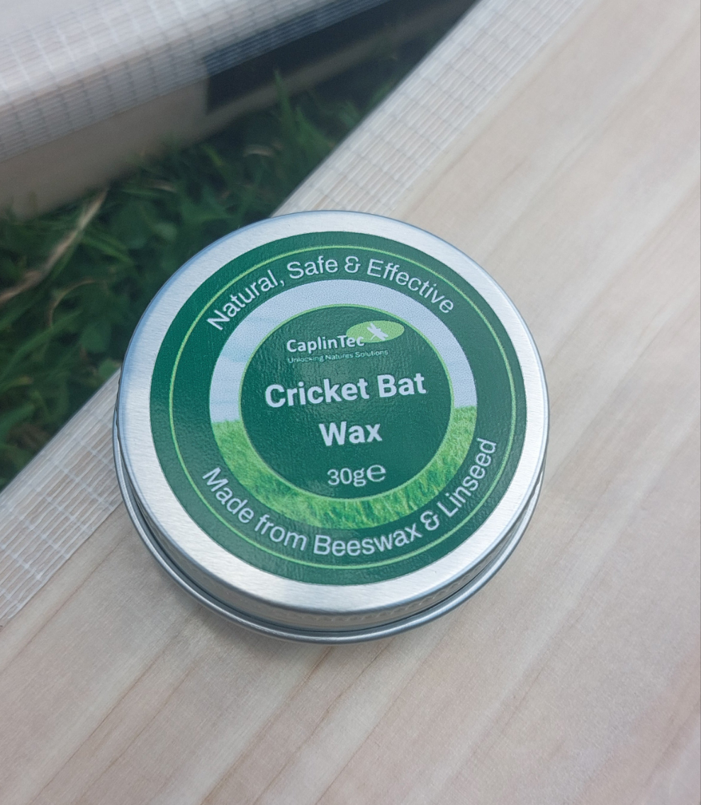 WC Cricket CaplinTec 30g tin of natural cricket bat wax on willow bat and grass background