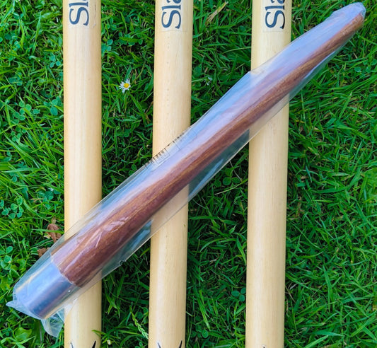 WC Cricket wooden cricket bat grip cone in clear plastic sleeve on grass beside wooden bat handles