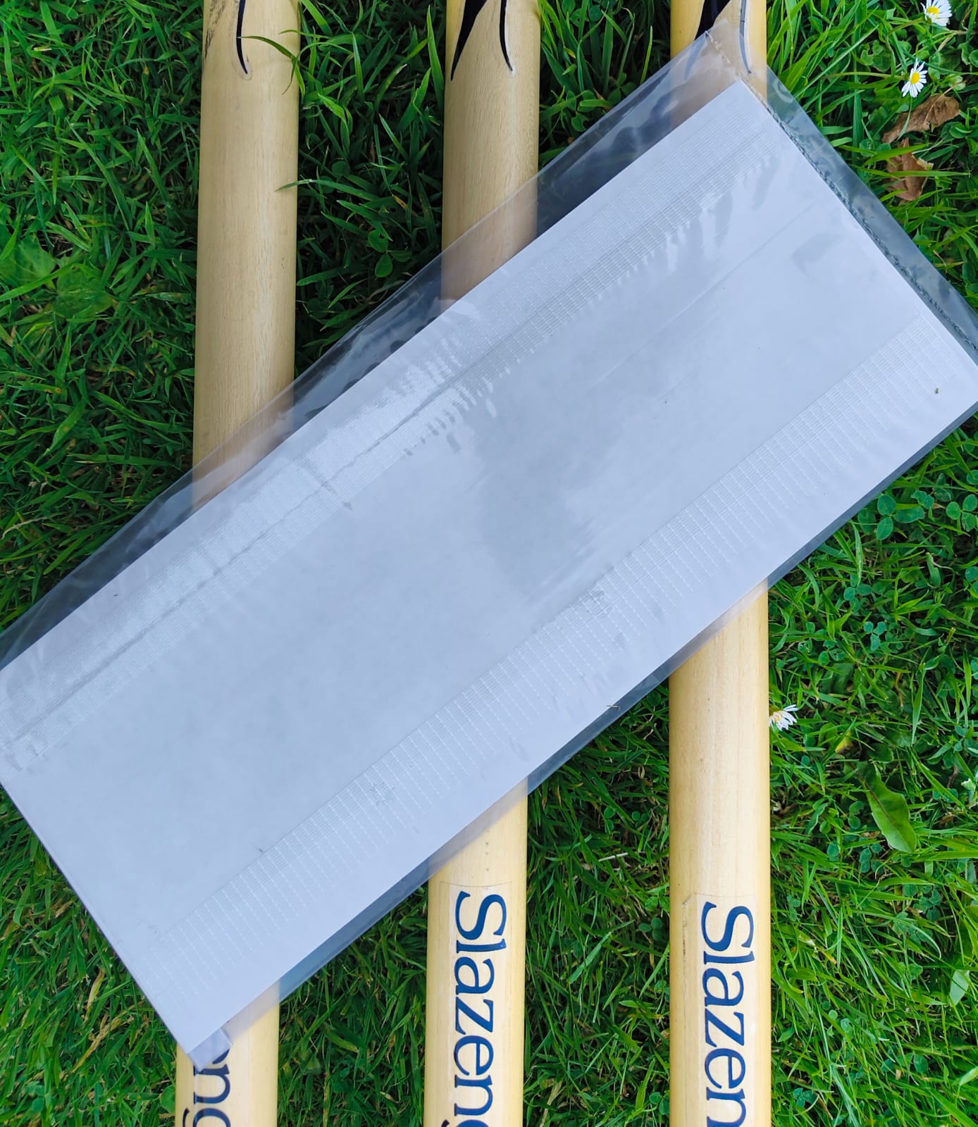 WC Cricket cricket bat anti scuff sheet in clear packaging laid across three Slazenger bats on grass